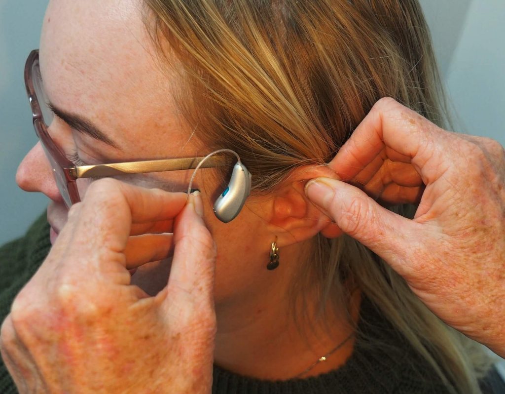 Una mujer introduciéndose suavemente un audífono en el oído, ajustándolo para obtener un sonido óptimo.